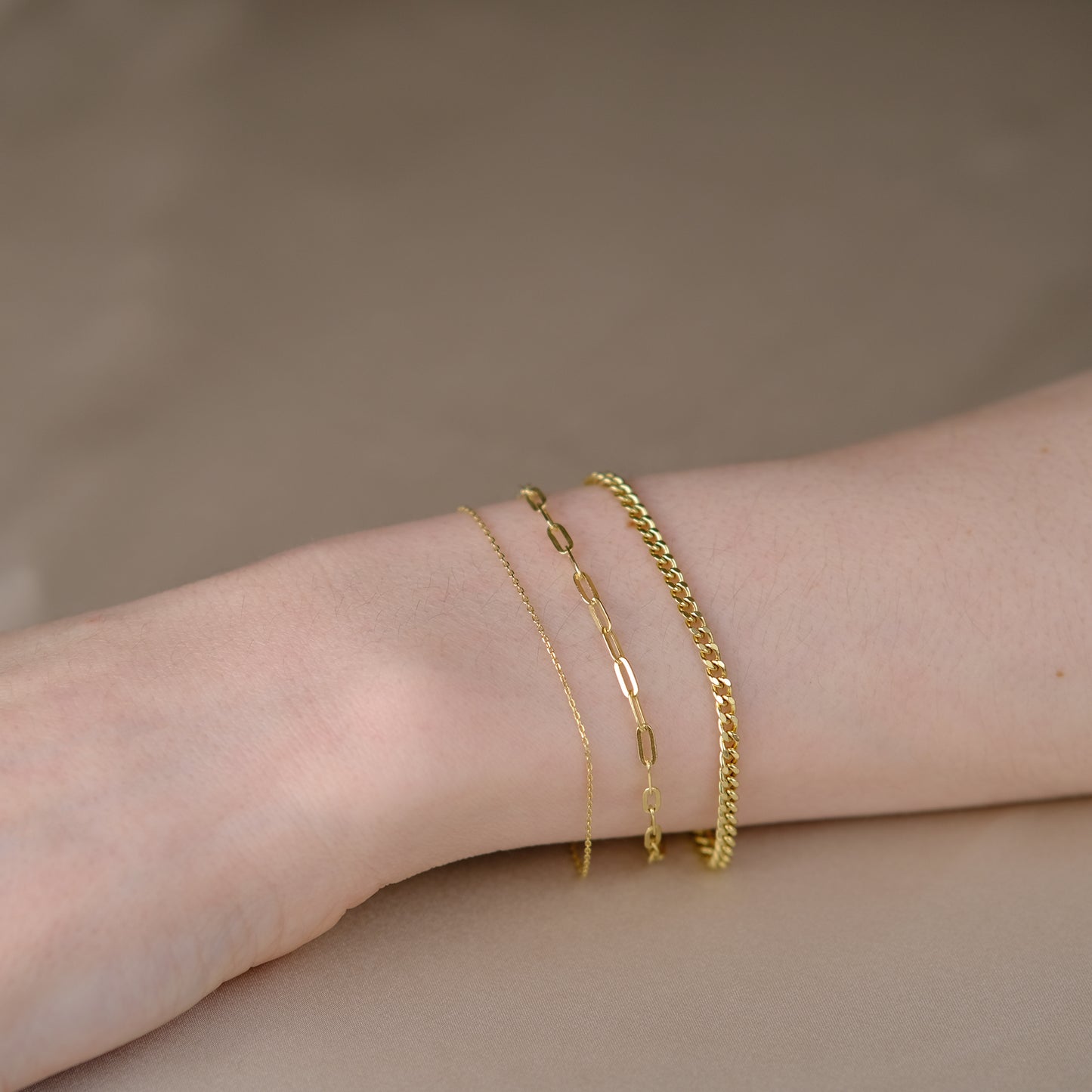 Handgelenk mit drei Armketten aus 14k Echtgold der Marke ayu – Essential Anchor Bracelet, Paperclip Bracelet & Curb Bracelet.