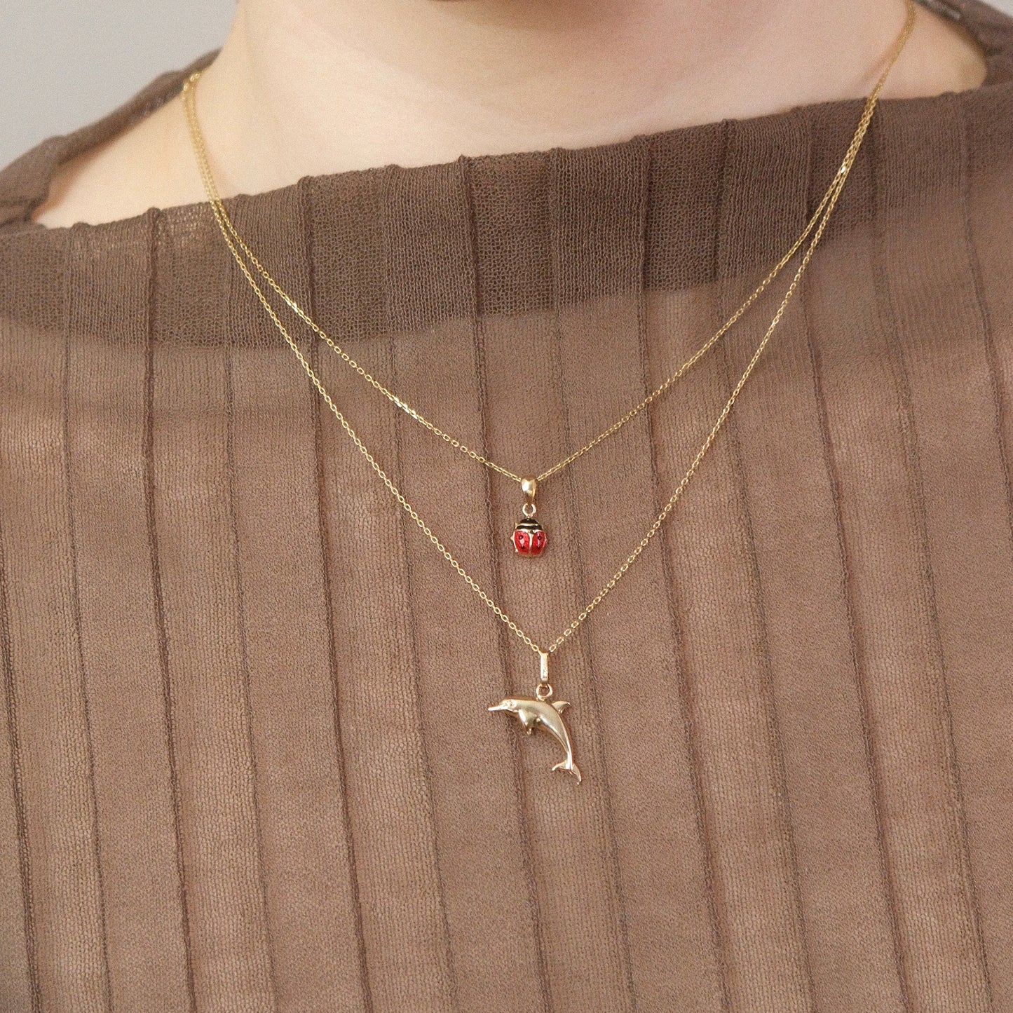 Model trägt eine Kette mit Delfin-Anhänger und darüber eine weitere Kette mit Marienkäfer-Anhänger aus 14k Echtgold.