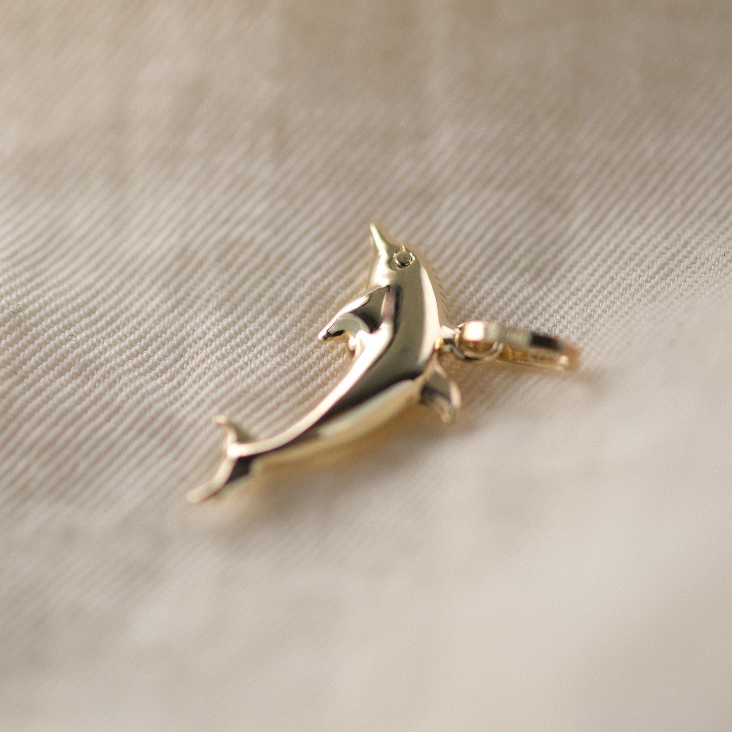 Seitenansicht eines Delfin-Anhängers aus 14k Echtgold auf beigem Untergrund.