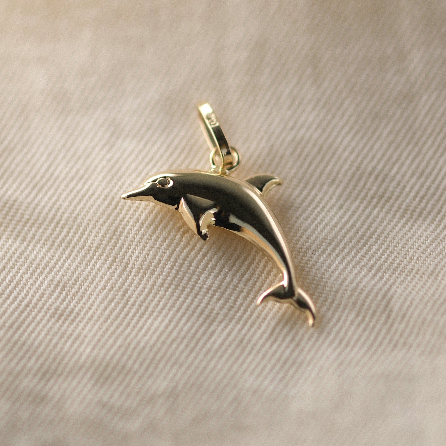 Delfin-Anhänger aus 14k Echtgold liegt auf beigem Untergrund.