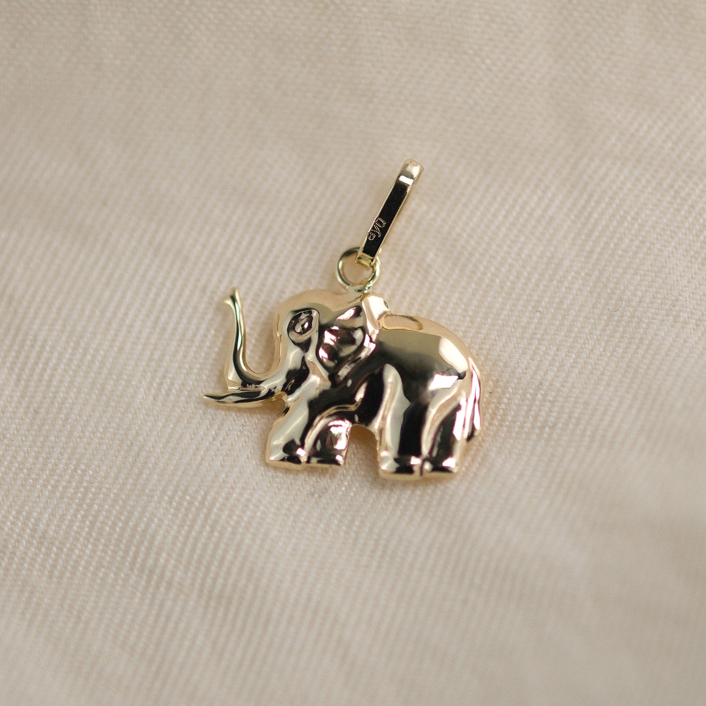 Elefant-Anhänger aus 14k Echtgold liegt auf beigem Untergrund.
