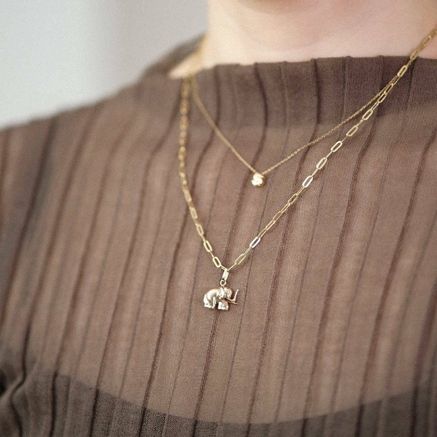 Model trägt eine Gliederkette mit Elefant-Anhänger aus 14k Echtgold und darüber eine weitere Kette mit dem Buchstaben-Anhänger „S“.