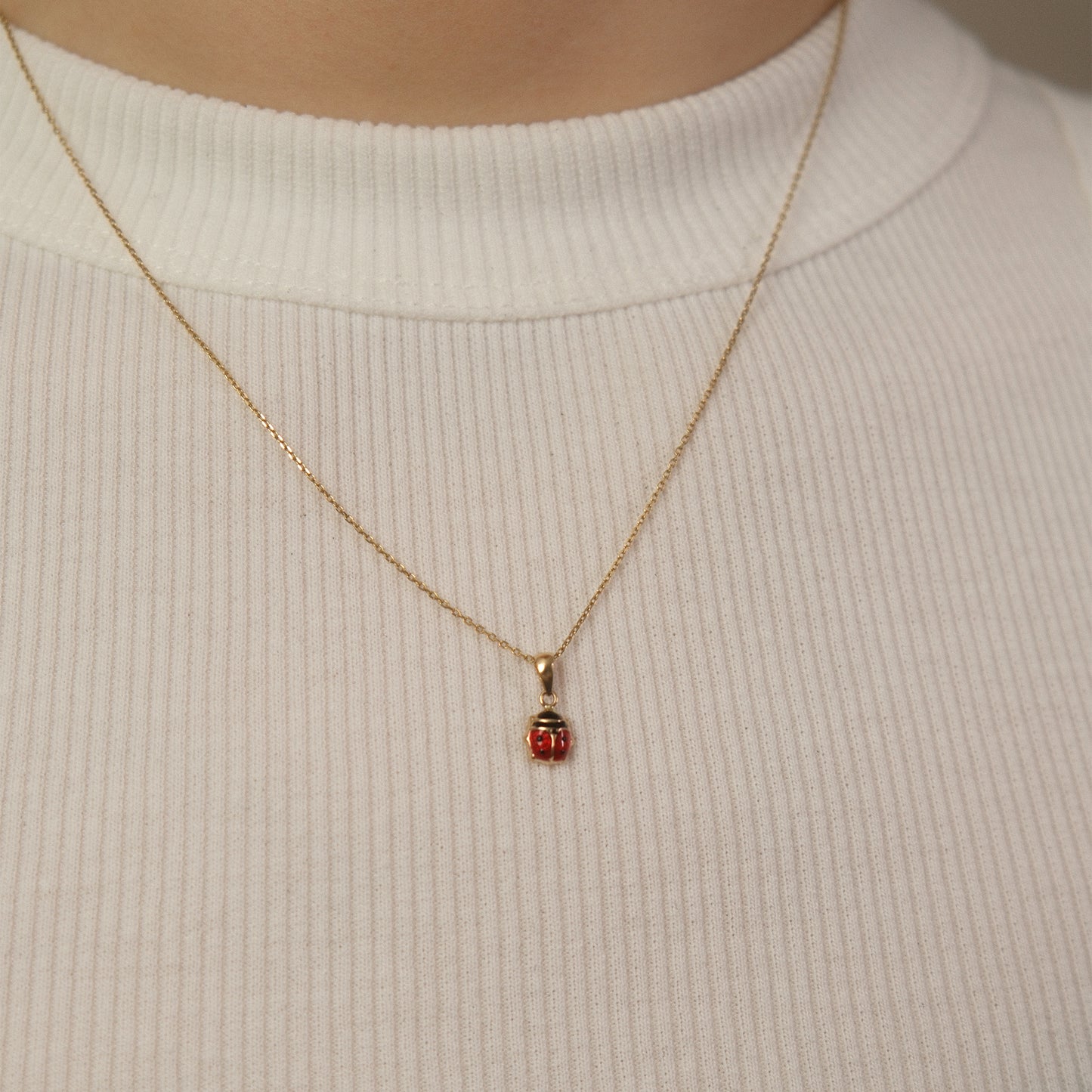 Model trägt eine Kette mit Marienkäfer-Anhänger aus 14k Echtgold über weißem Top.
