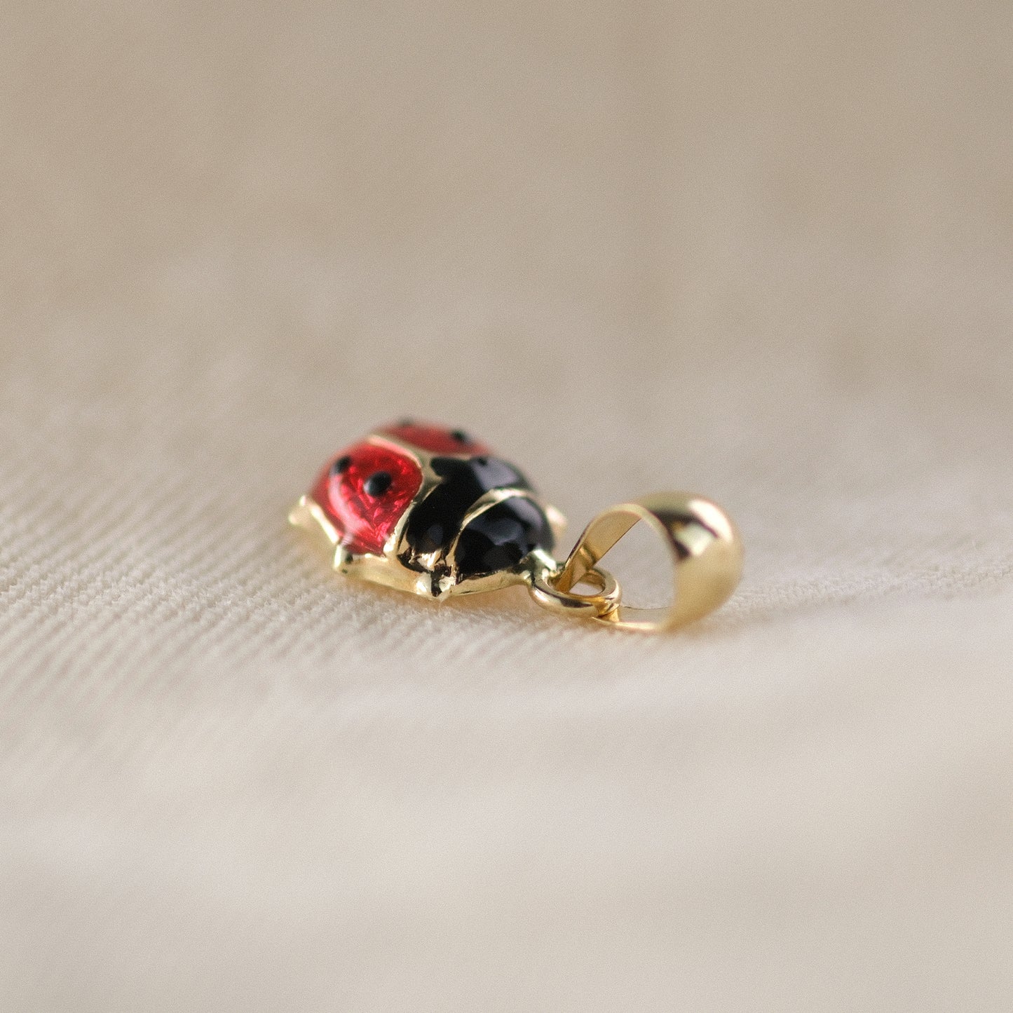 Seitenansicht eines Marienkäfer-Anhängers aus 14k Echtgold auf beigem Untergrund.