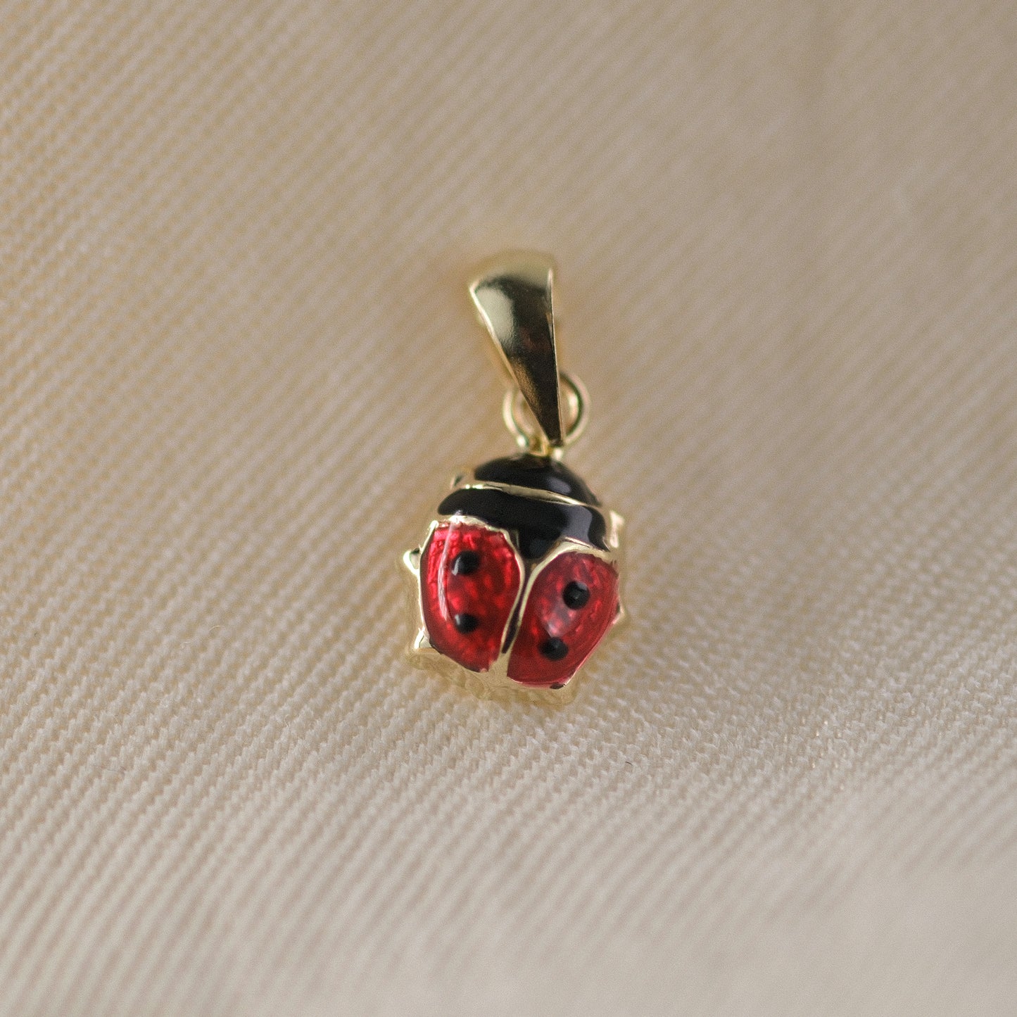 Marienkäfer-Anhänger aus 14k Echtgold liegt auf beigem Untergrund.