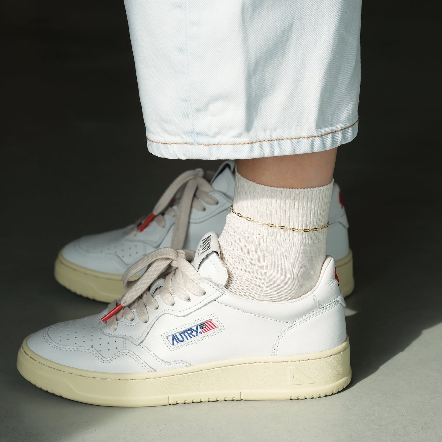 Model trägt weiße Sneaker mit weißen Socken und darüber ein goldenes Fußkettchen aus 14k Gold der Marke ayu.