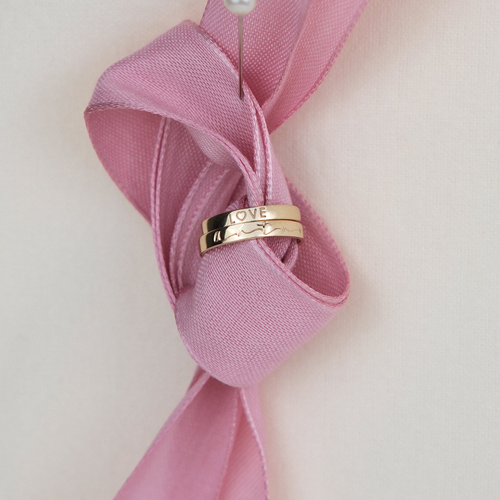 Bandring aus 14k Echtgold mit Hand-Gravur dekoriert an rosa Schleife.