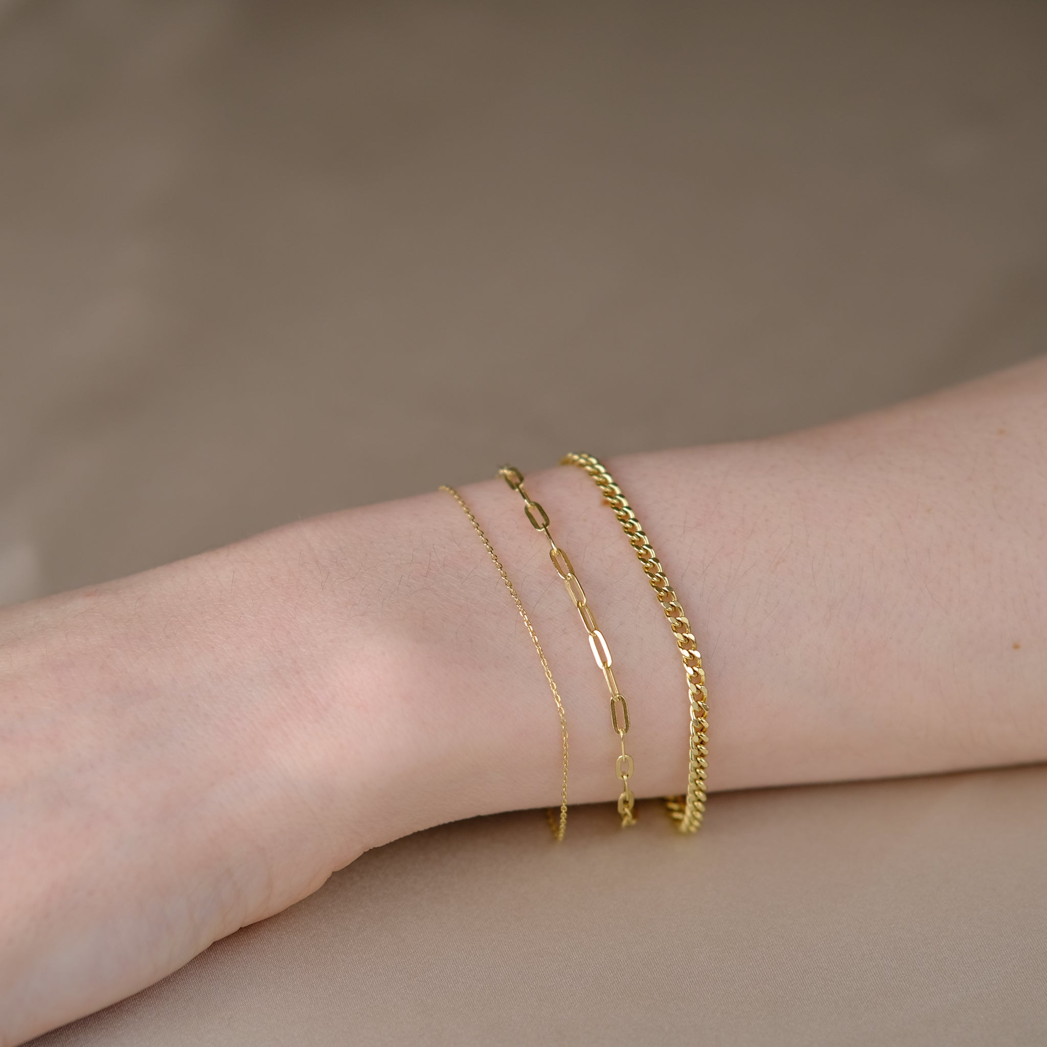 Handgelenk mit drei Armketten aus 14k Echtgold der Marke ayu – Essential Anchor Bracelet, Paperclip Bracelet & Curb Bracelet.