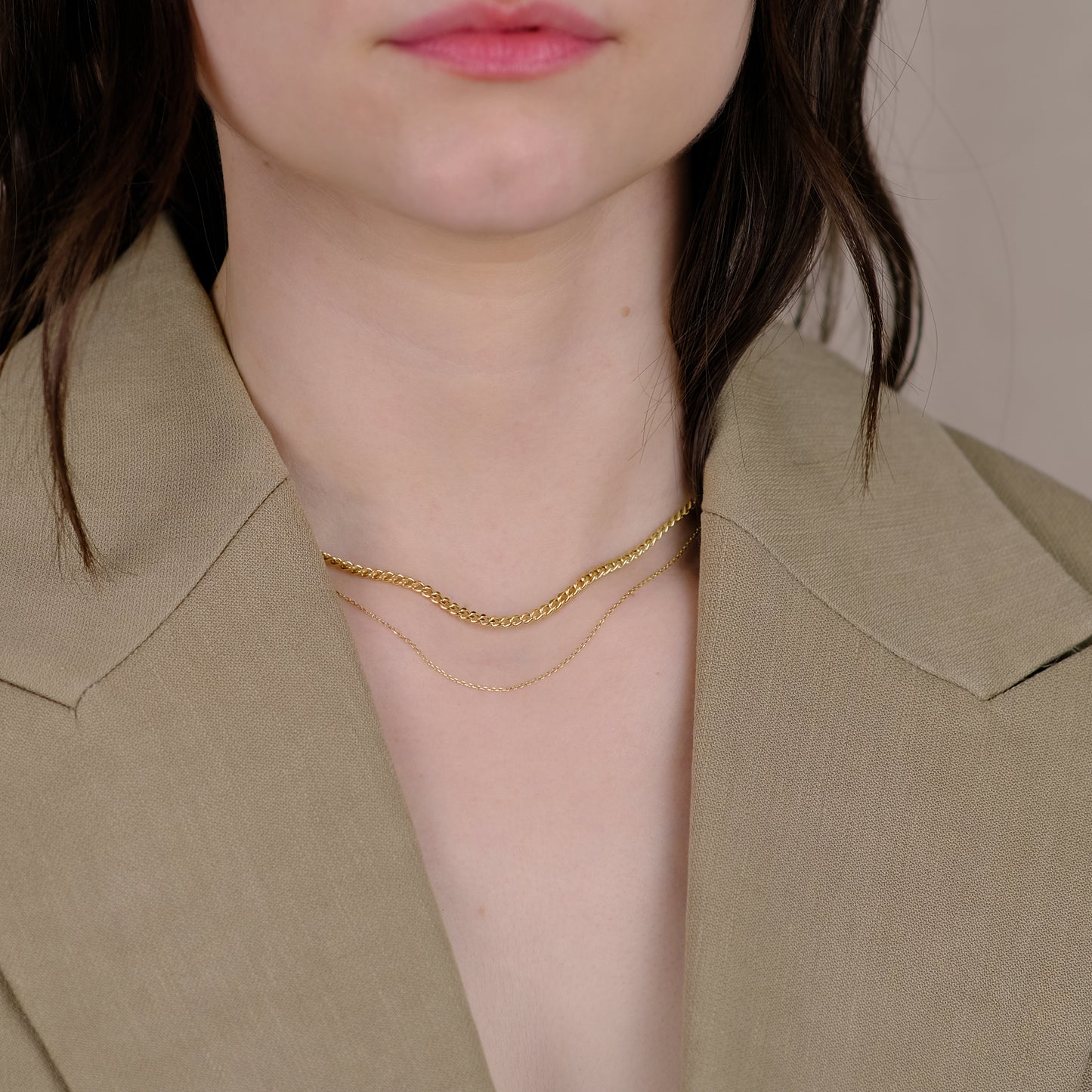 Frau trägt einen braunen Blazer und die Curb Chain Necklace aus 14k Echtgold in Kombination mit der Essential Anchor Chain Necklace.