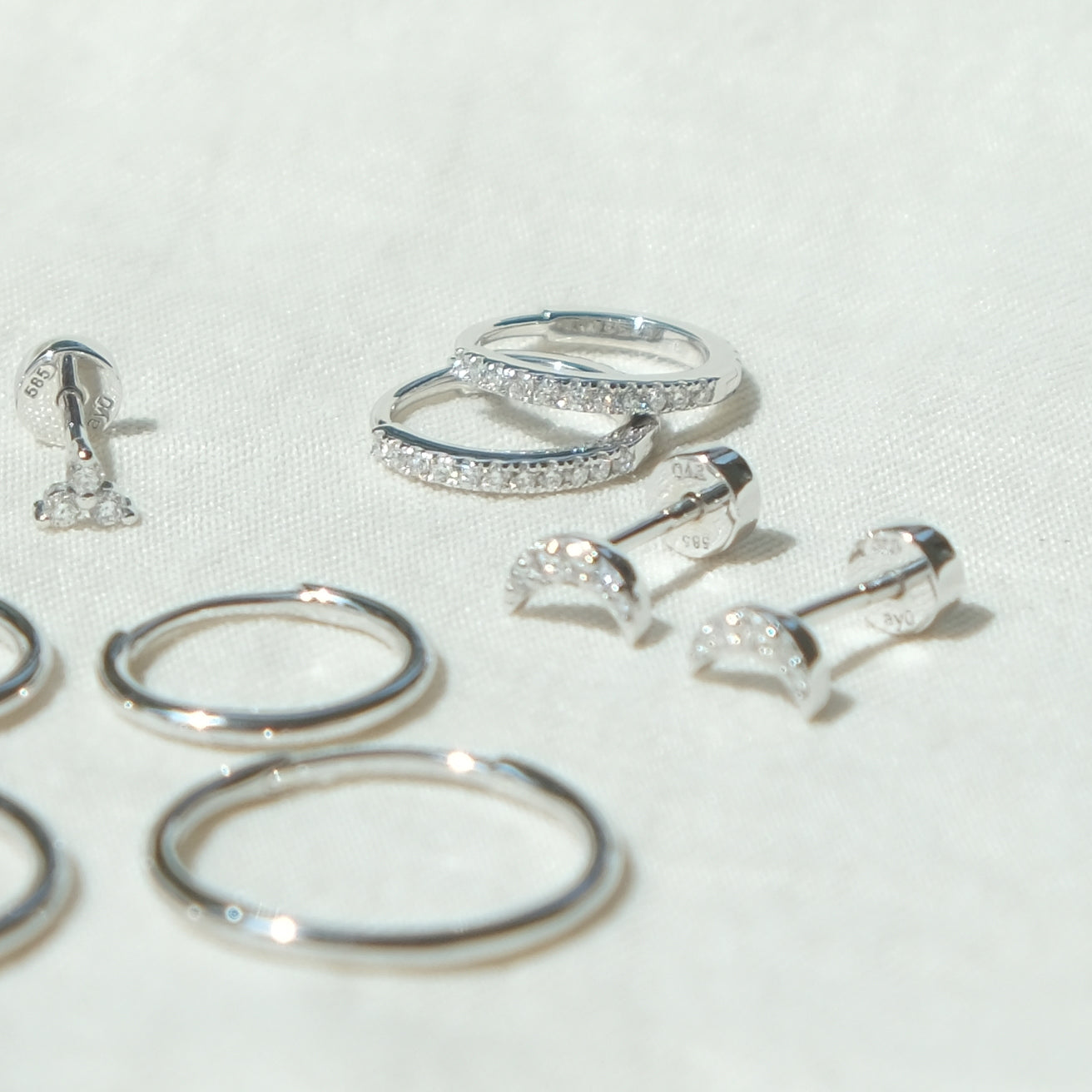 Ein Paar des Diamond Eternity Huggies aus 14k Weißgold und 22 Diamanten liegend auf weißem Untergrund.