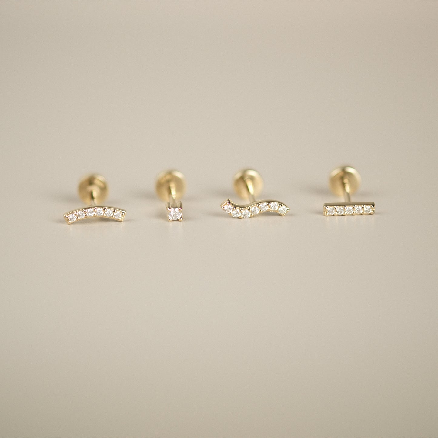 Vier Diamantohrstecker aus 14k Gold liegen nebeneinander auf beigem Untergrund.