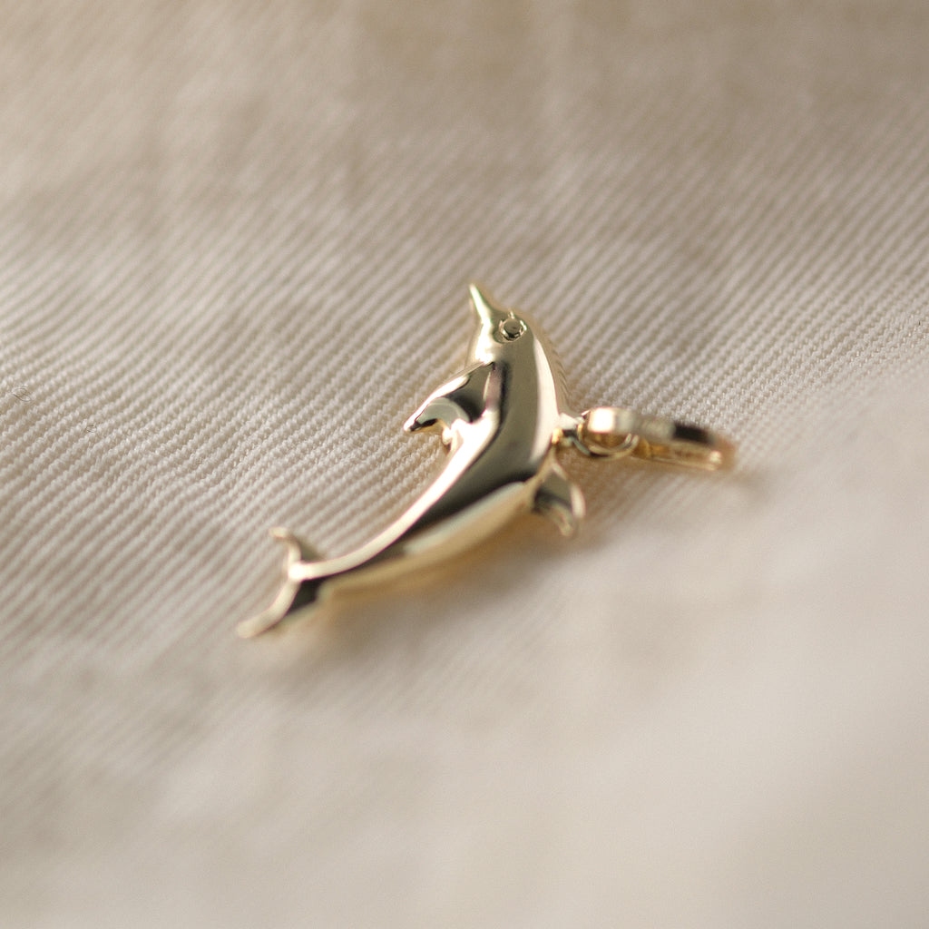 Seitenansicht eines Delfin-Anhängers aus 14k Echtgold auf beigem Untergrund.