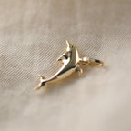 Seitenansicht eines Delfin-Anhängers aus 14k Echtgold auf beigem Untergrund.