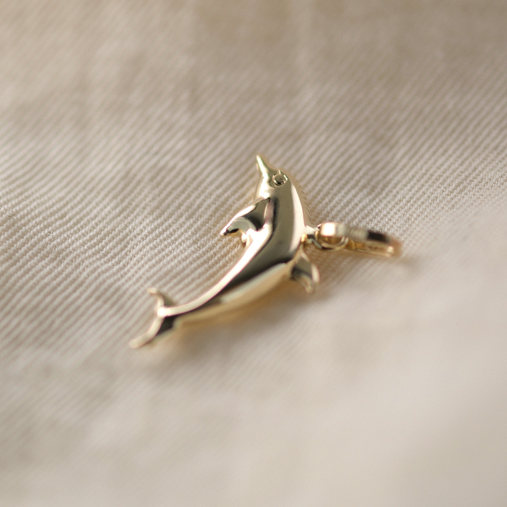 Seitenansicht eines Delfin-Anhängers aus 14k Echtgold auf beigem Untergrund.