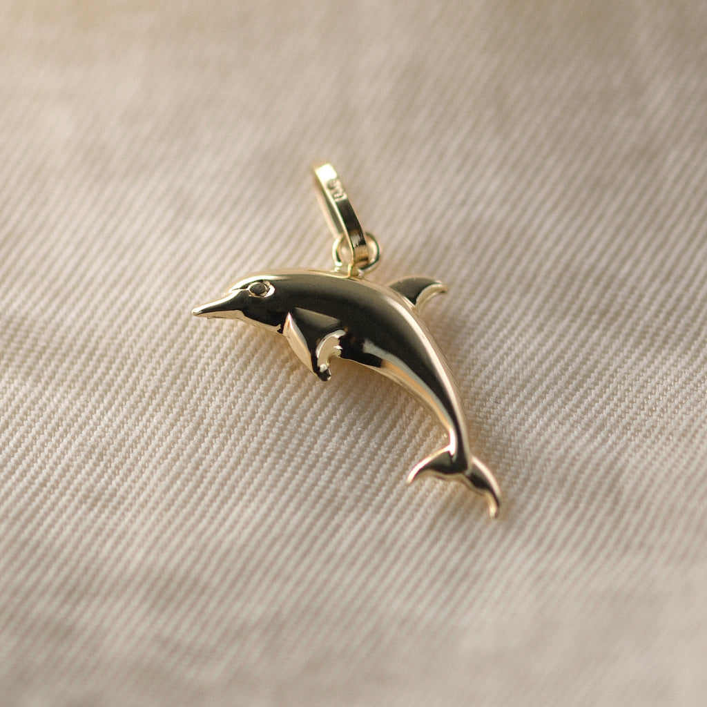 Delfin-Anhänger aus 14k Echtgold liegt auf beigem Untergrund.