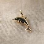 Delfin-Anhänger aus 14k Echtgold liegt auf beigem Untergrund.