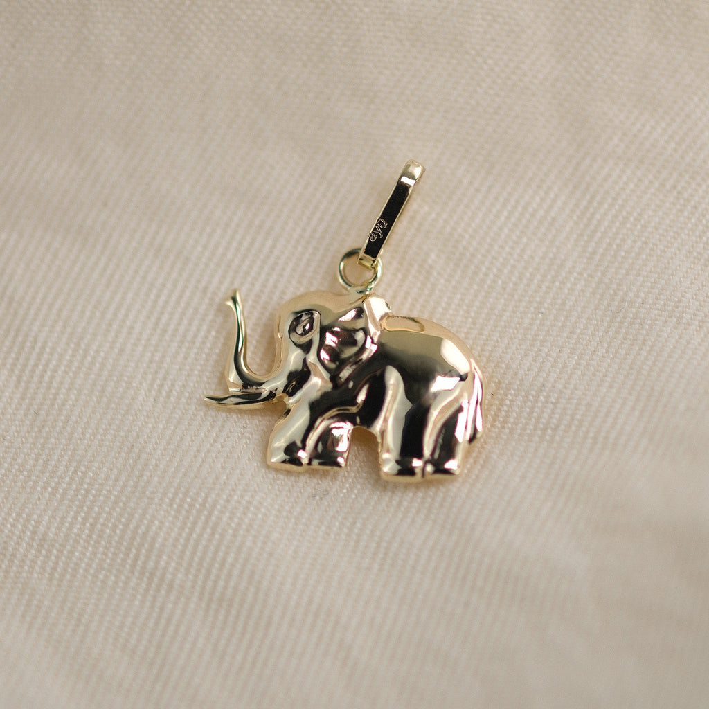 Elefant-Anhänger aus 14k Echtgold liegt auf beigem Untergrund.