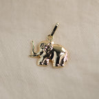 Elefant-Anhänger aus 14k Echtgold liegt auf beigem Untergrund.