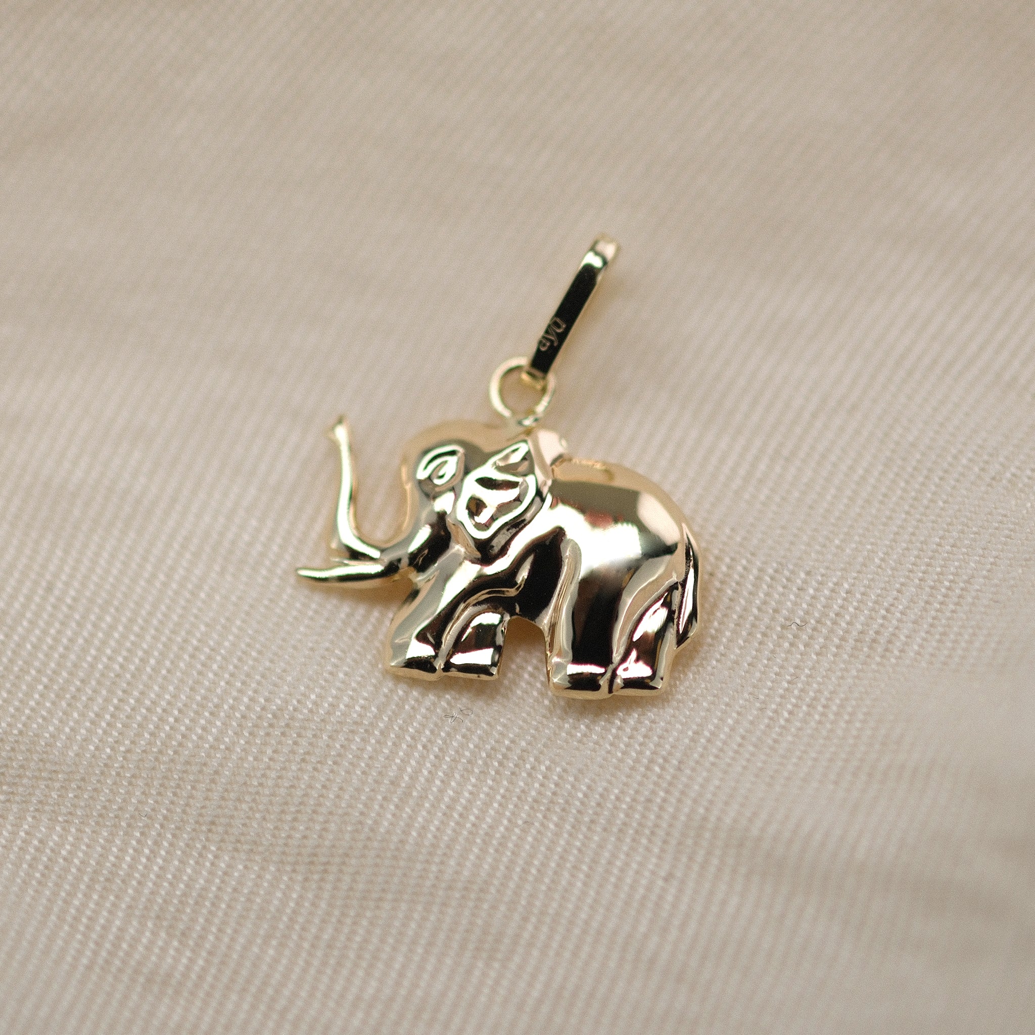 Elefant-Anhänger aus 14k Echtgold auf beigem Untergrund.
