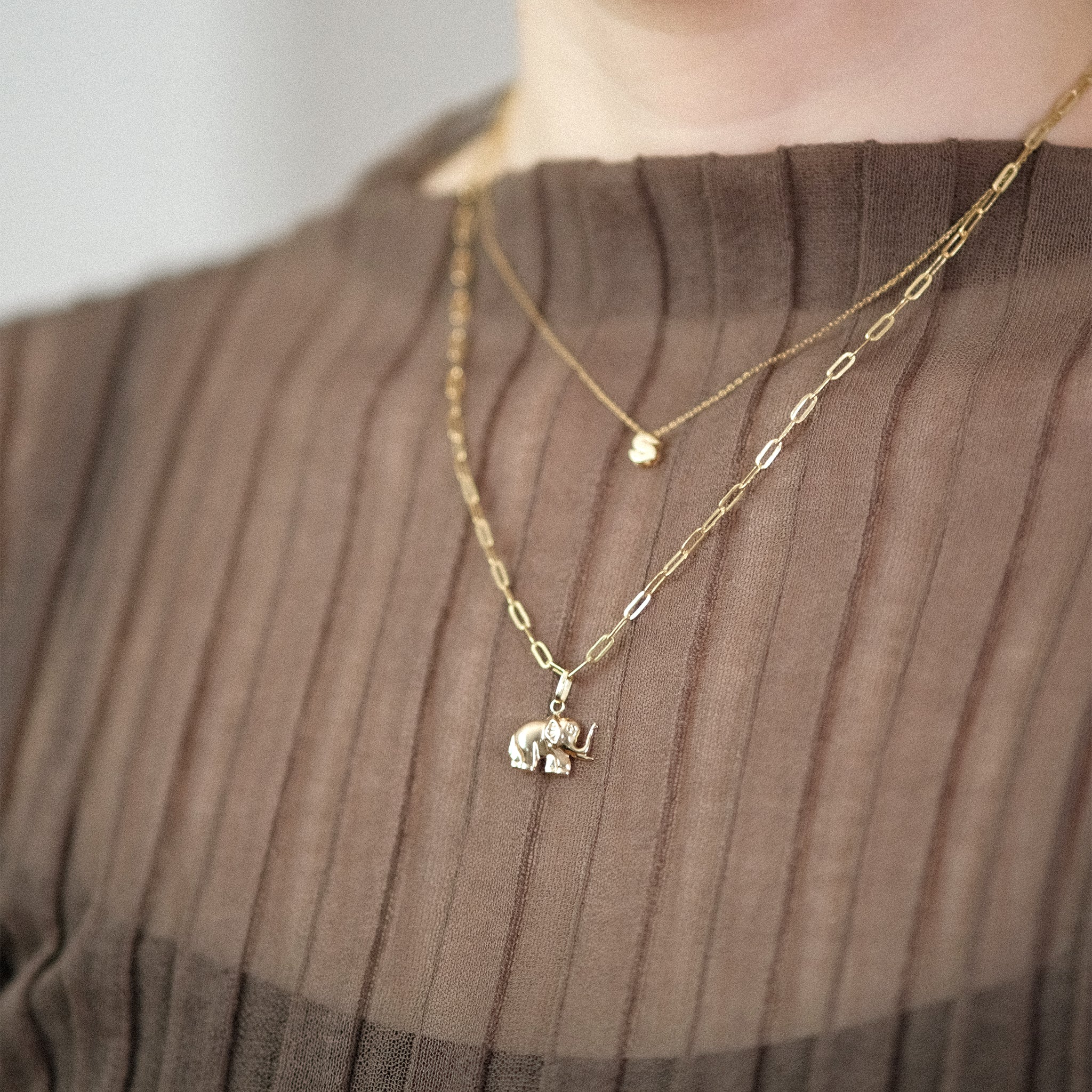 Model trägt eine Gliederkette mit Elefant-Anhänger aus 14k Echtgold und darüber eine weitere Kette mit dem Buchstaben-Anhänger „S“.