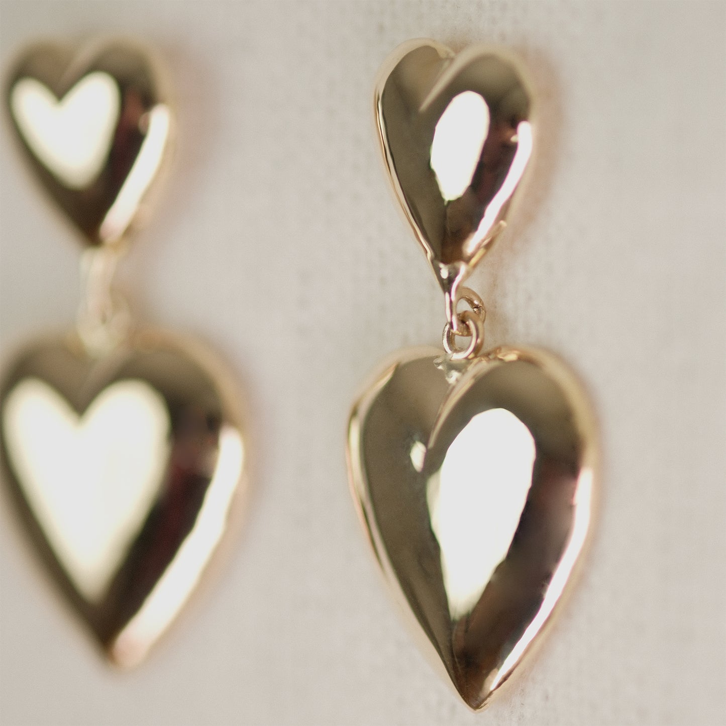 Nahaufnahme der Heart Drop Earrings aus 14k Echtgold vor beigem Hintergrund.