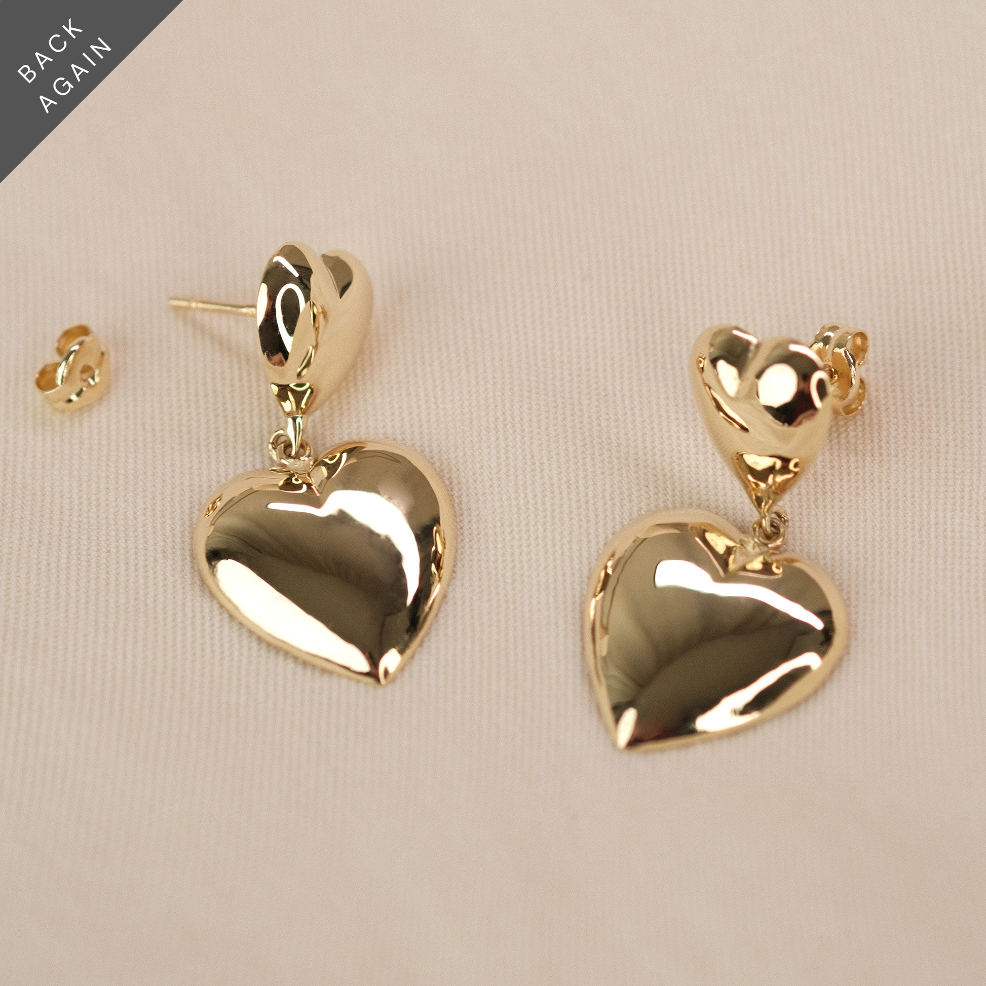 Herzohrringe aus 14k Echtgold liegen auf beigem Untergrund.