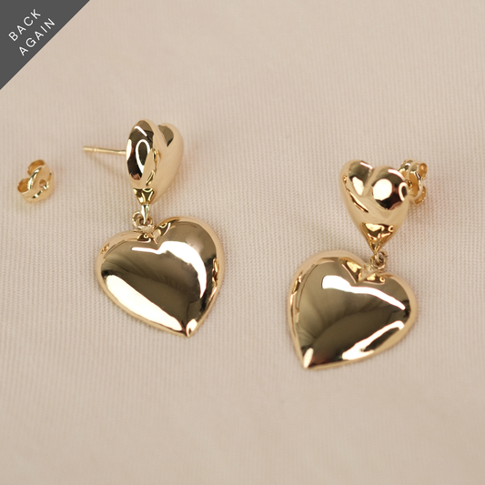 Herzohrringe aus 14k Echtgold liegen auf beigem Untergrund.
