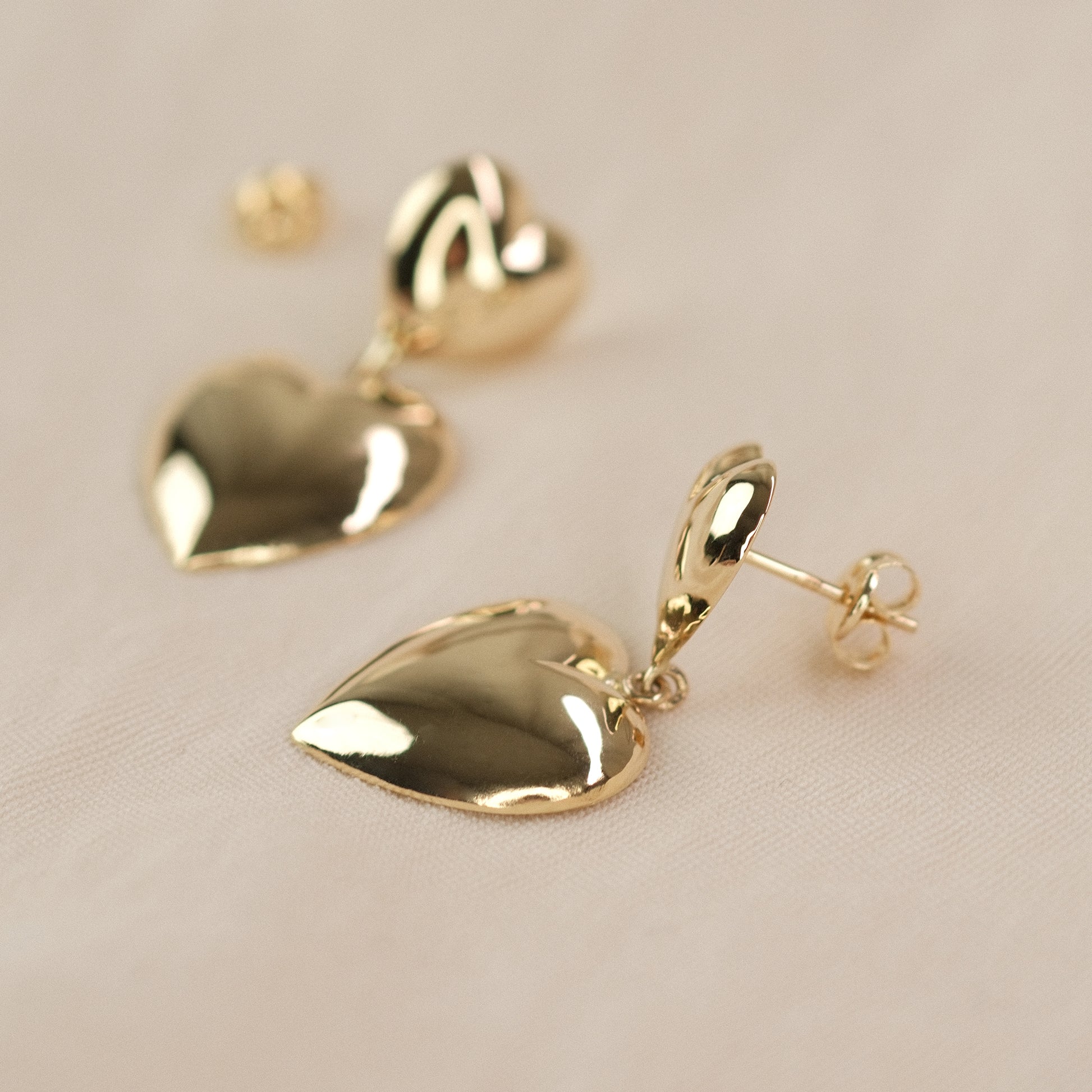 Herzohrringe aus 14k Echtgold liegen auf beigem Untergrund.