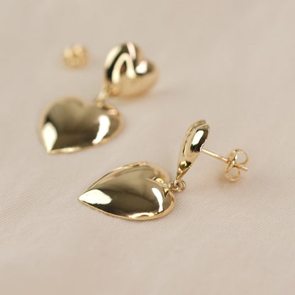 Herzohrringe aus 14k Echtgold liegen auf beigem Untergrund.