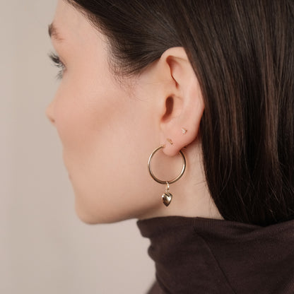 Model trägt die Classic Hoop Earrings Large mit dem Heart Pendant aus 14k Gold als Einhänger.