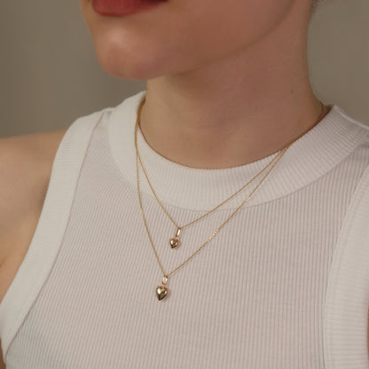 Model trägt eine Kette mit Herz-Anhänger und darüber eine weitere Kette mit kleinem Herz-Anhänger aus 14k Echtgold.