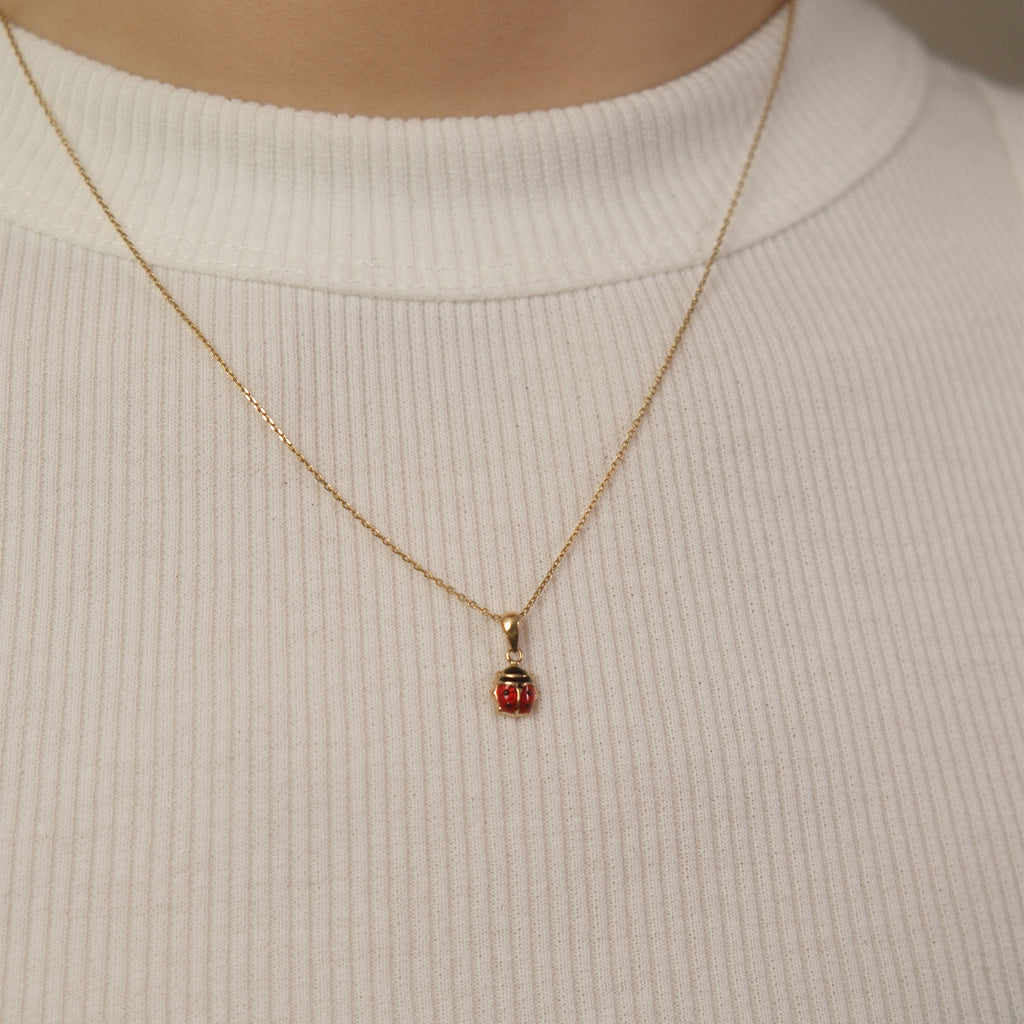 Model trägt eine Kette mit Marienkäfer-Anhänger aus 14k Echtgold über weißem Top.