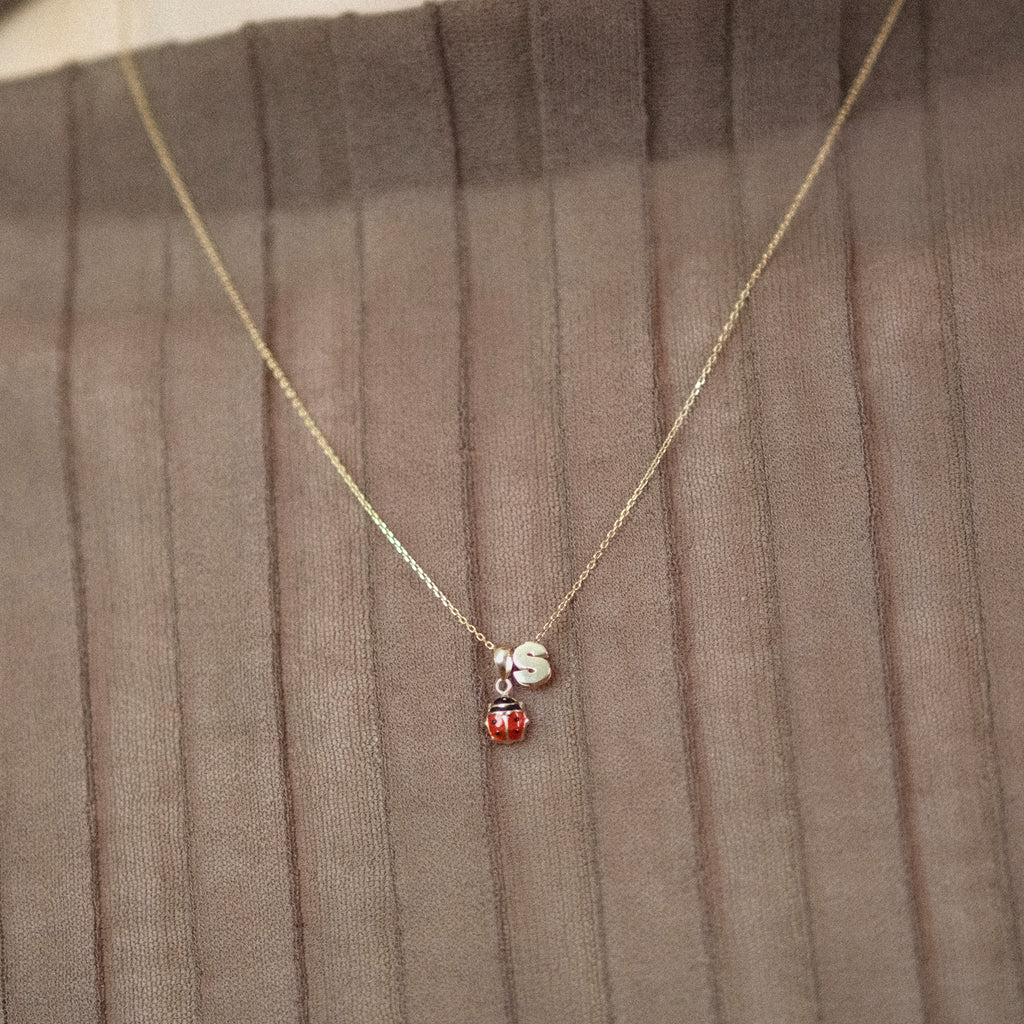 Model trägt eine Kette mit Marienkäfer-Anhänger und dem Buchstaben-Anhänger „S“ aus 14k Echtgold.