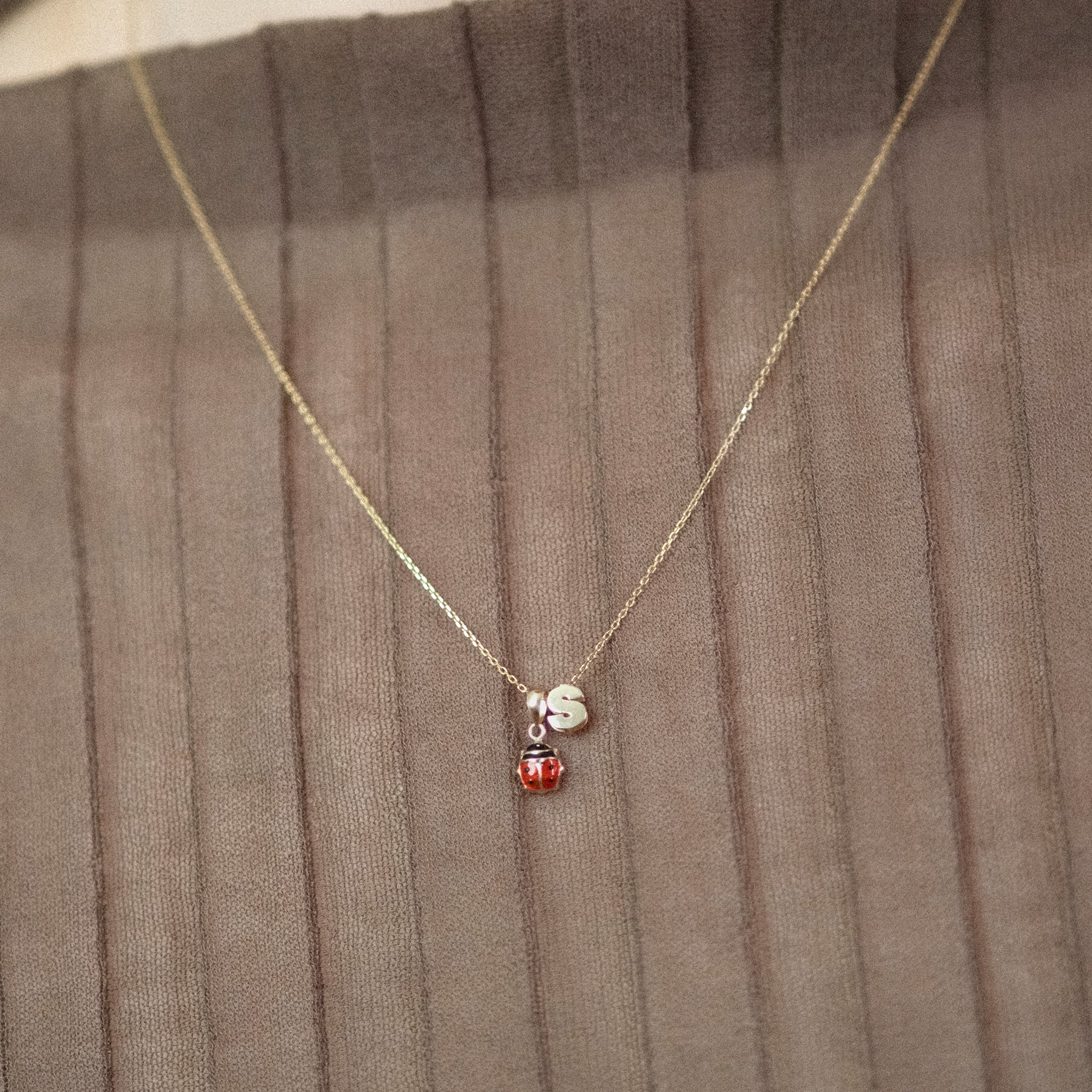 Model trägt eine Kette mit Marienkäfer-Anhänger und dem Buchstaben-Anhänger „S“ aus 14k Echtgold.