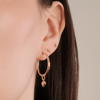 Model trägt die Classic Hoop Earrings Large mit dem Mini Heart Pendant aus 14k Gold als Einhänger.