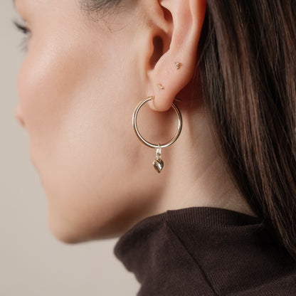 Seitenansicht: Model trägt die Classic Hoop Earrings Large mit dem Mini Heart Pendant aus 14k Gold als Einhänger.