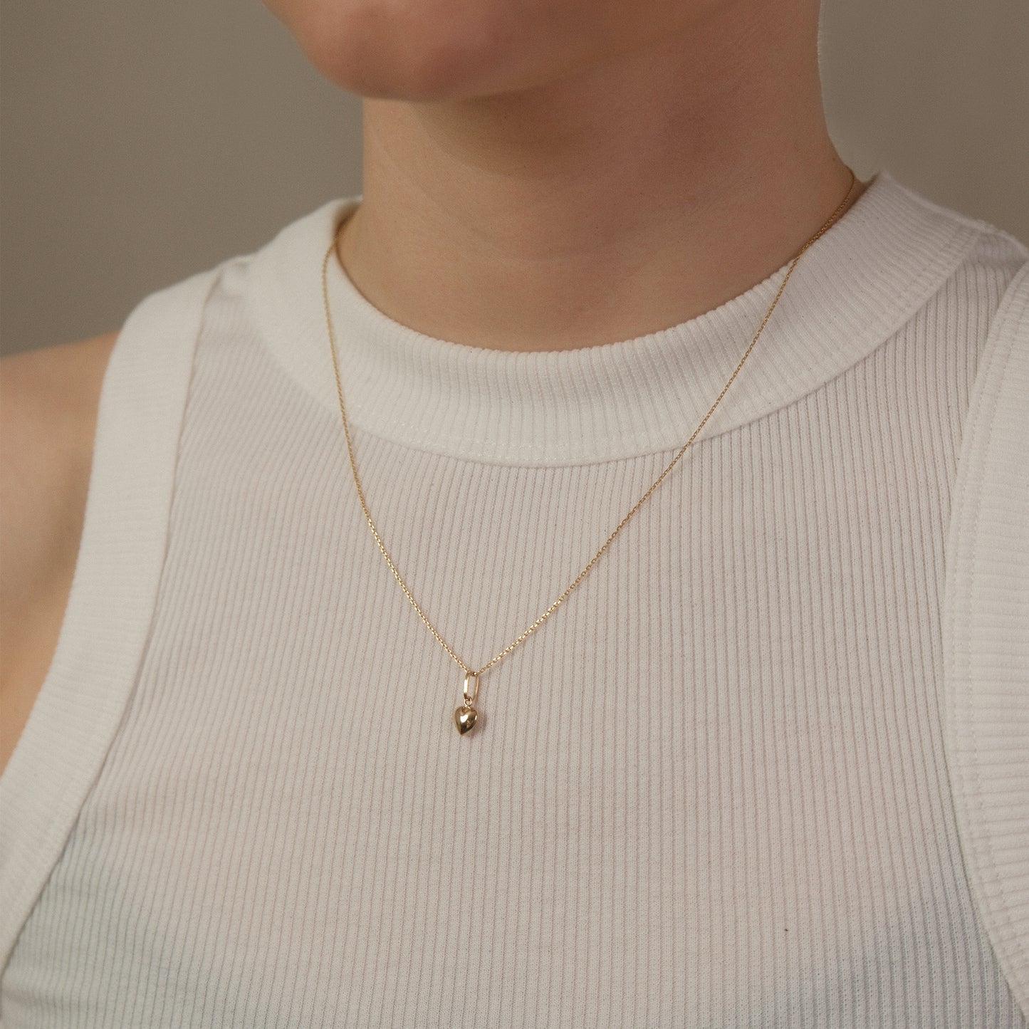 Model trägt eine Kette mit kleinem Herz-Anhänger aus 14k Echtgold über weißem Top.