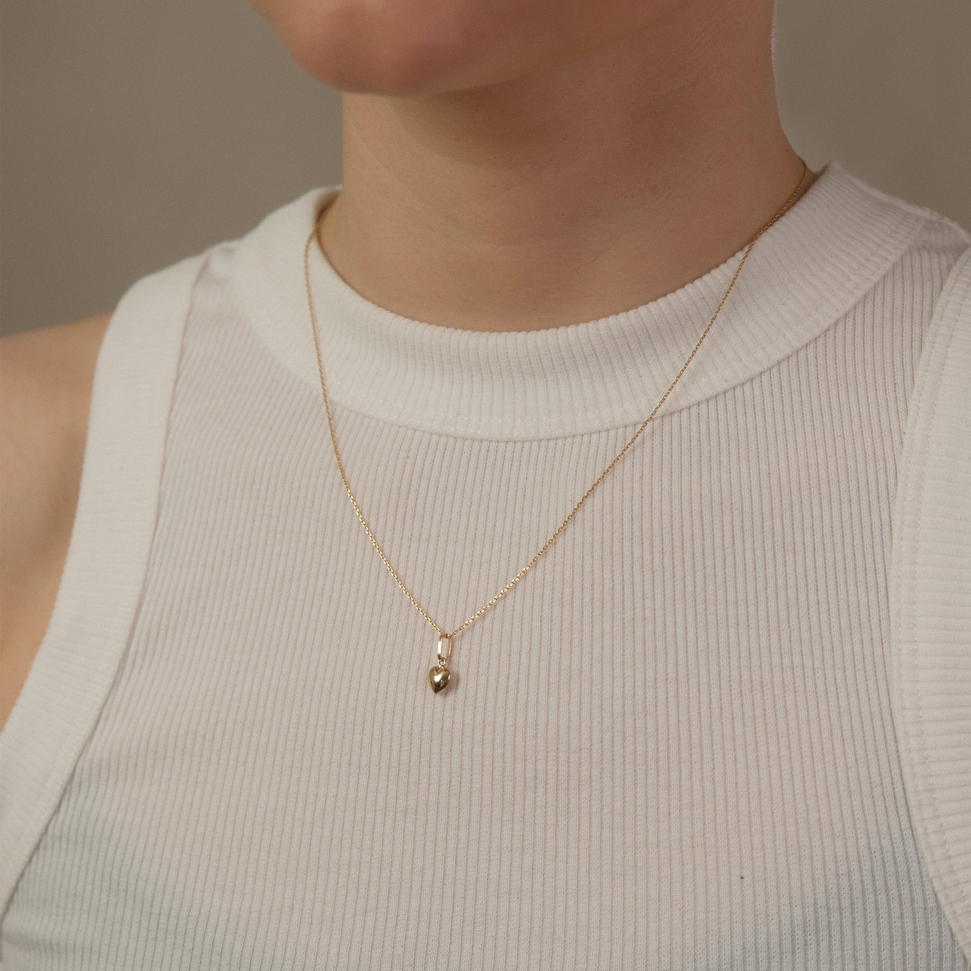 Model trägt eine Kette mit kleinem Herz-Anhänger aus 14k Echtgold über weißem Top.