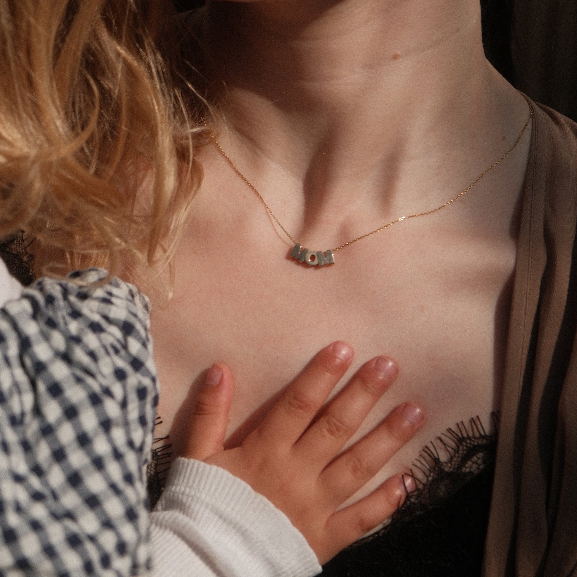 Model trägt eine MOM-Buchstabenkette aus 14k Echtgold mit Kind auf dem Arm.