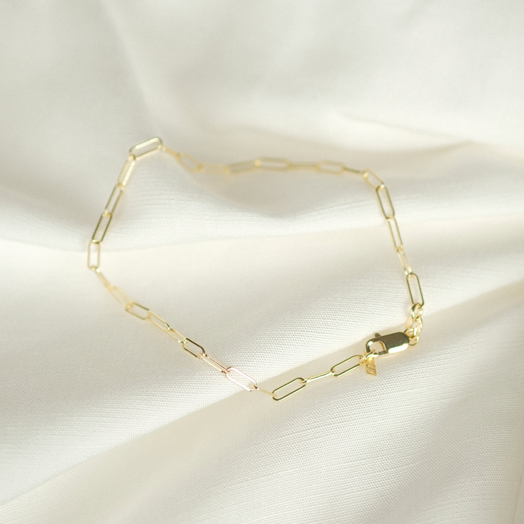 Elegantes Paperclip-Fußkettchen aus 14k Massivgold, flach liegend auf weißem Stoff.