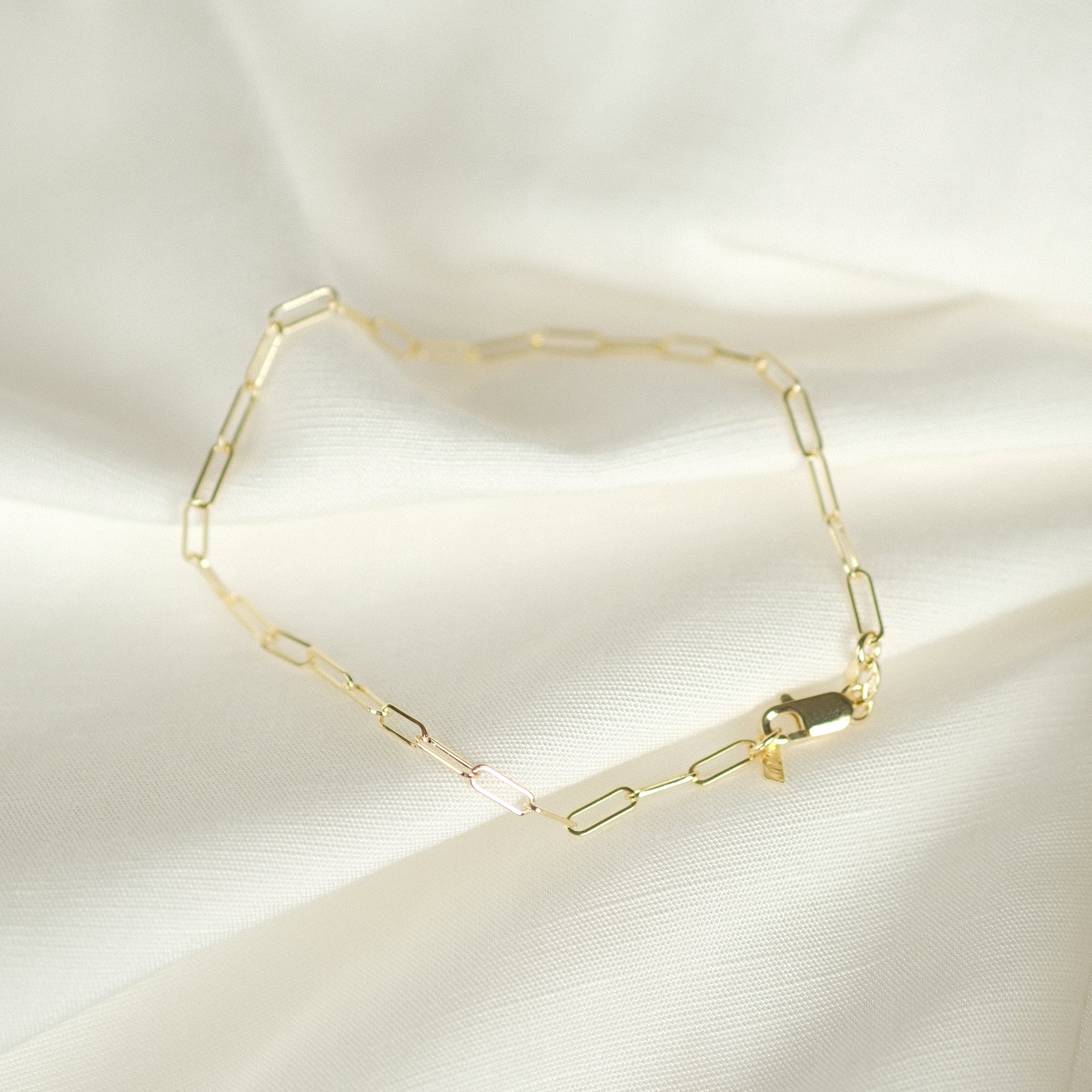 Elegantes Paperclip-Fußkettchen aus 14k Massivgold, flach liegend auf weißem Stoff.