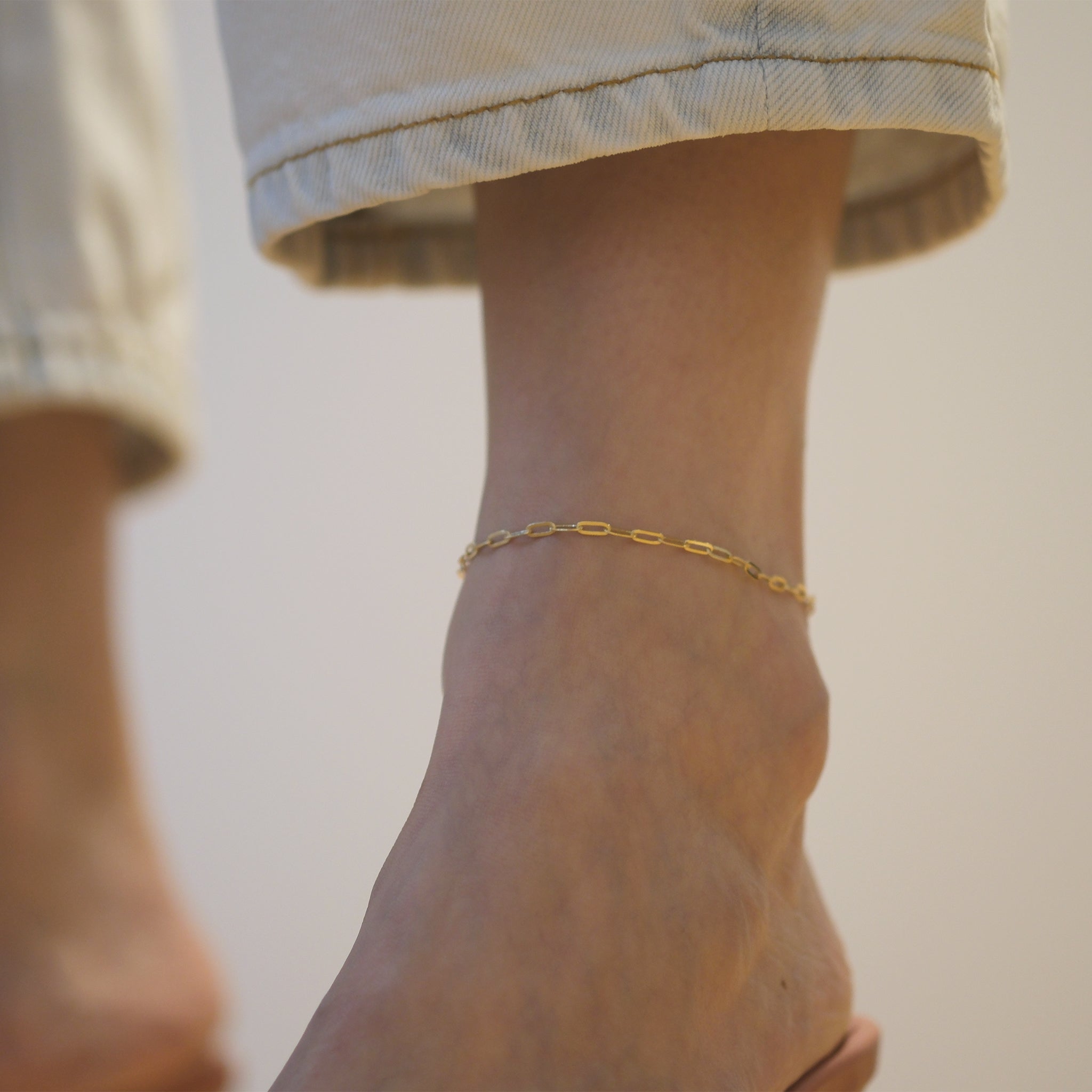 Model trägt Paperclip Chain Anklet aus 14k Echtgold.
