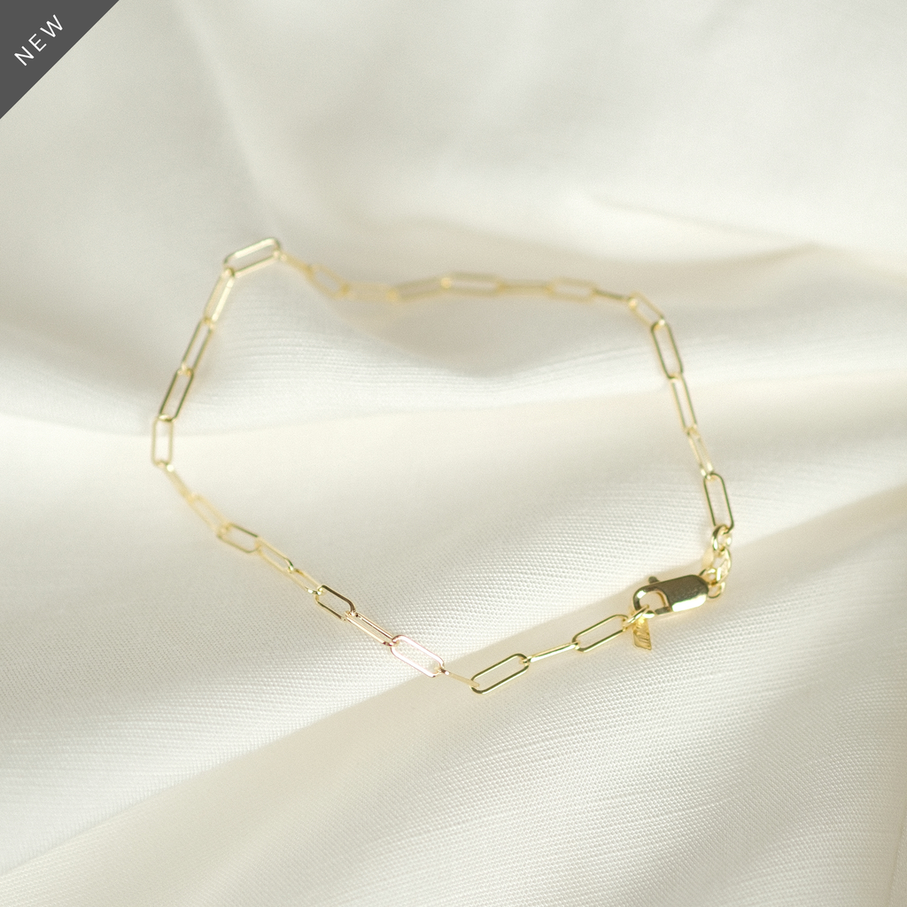 Elegantes Paperclip-Armband aus 14k Gold, flach liegend auf weißem Stoff, ideal als Geschenk.
