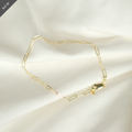Elegantes Paperclip-Armband aus 14k Gold, flach liegend auf weißem Stoff, ideal als Geschenk.
