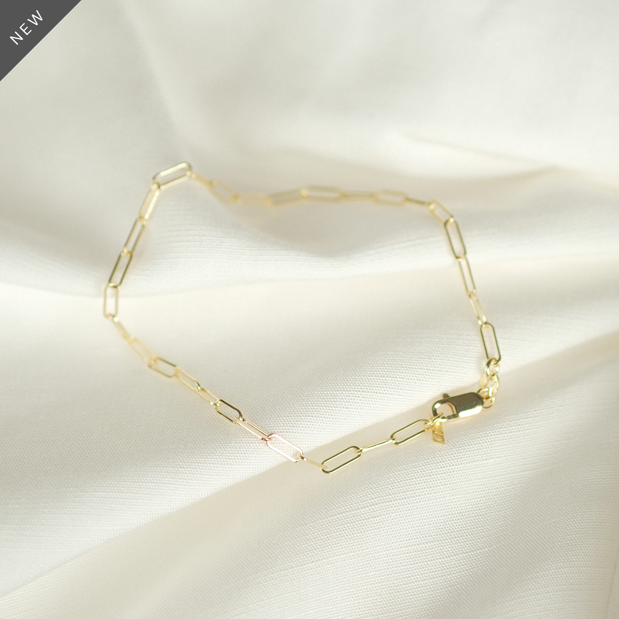 Elegantes Paperclip-Armband aus 14k Gold, flach liegend auf weißem Stoff, ideal als Geschenk.