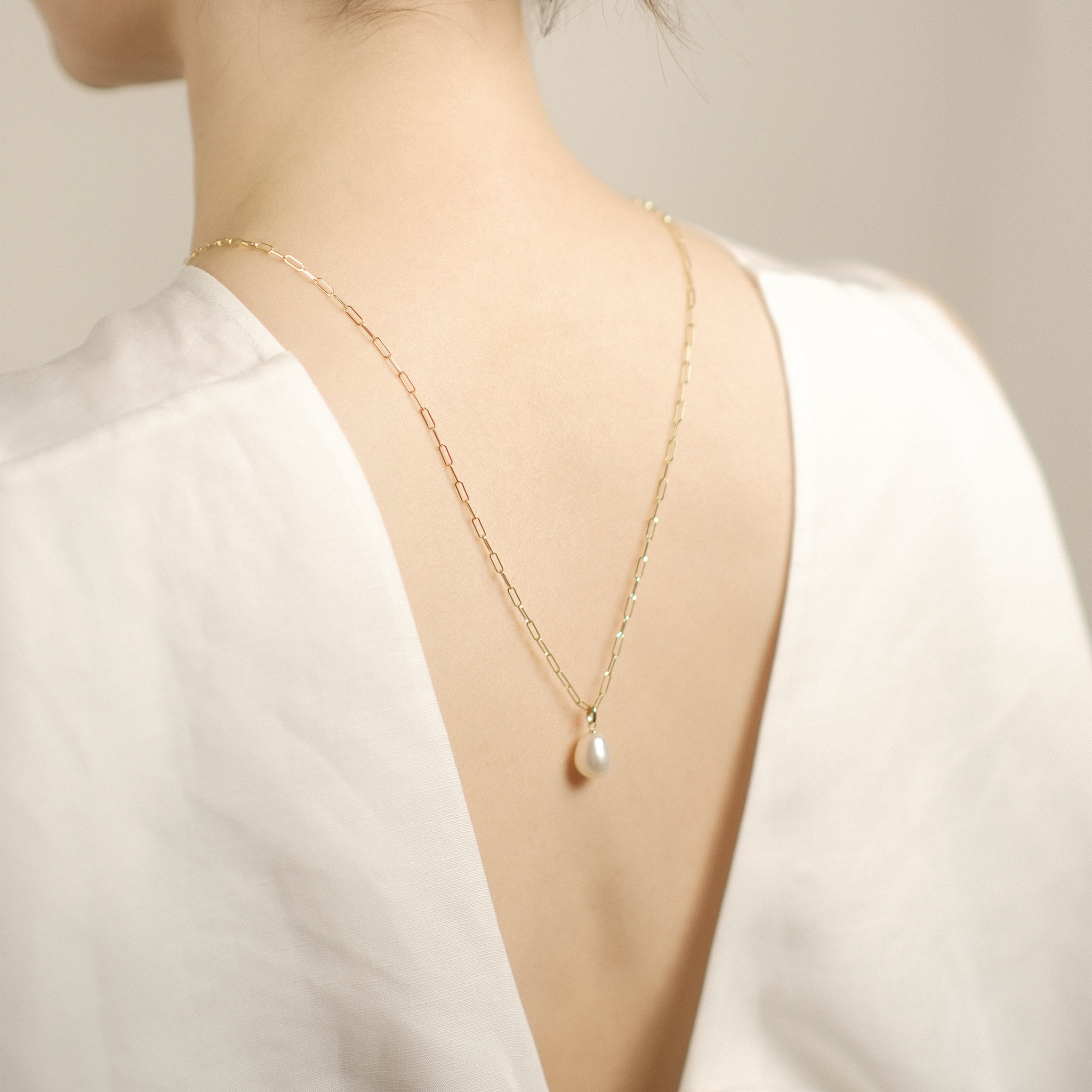Model trägt elegante Paperclip-Kette aus 14k Gold mit Perlenanhänger im Rückenausschnitt.