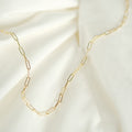 Elegante Paperclip-Kette aus 14k Gold, flach liegend auf weißem Stoff.