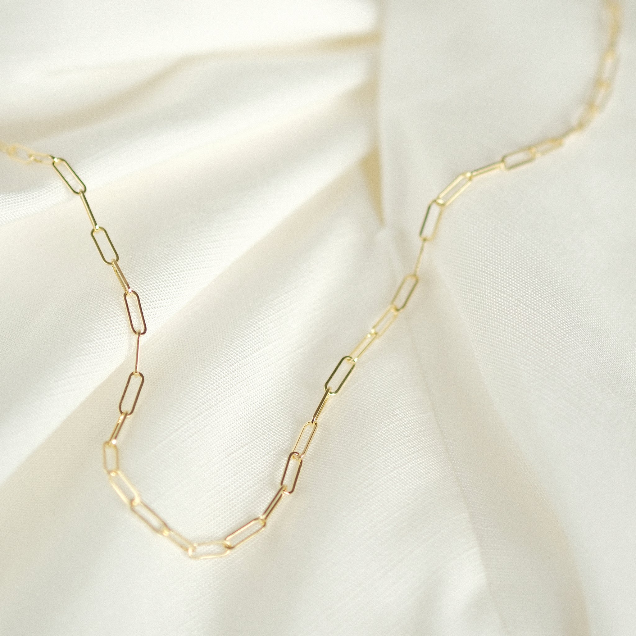 Elegante Paperclip-Kette aus 14k Gold, flach liegend auf weißem Stoff.