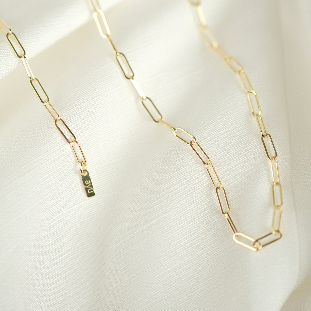 Elegante Paperclip-Kette aus 14k Gold, drapiert auf weißem Stoff, ideal als Geschenk.