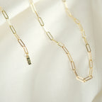 Elegante Paperclip-Kette aus 14k Gold, drapiert auf weißem Stoff, ideal als Geschenk.